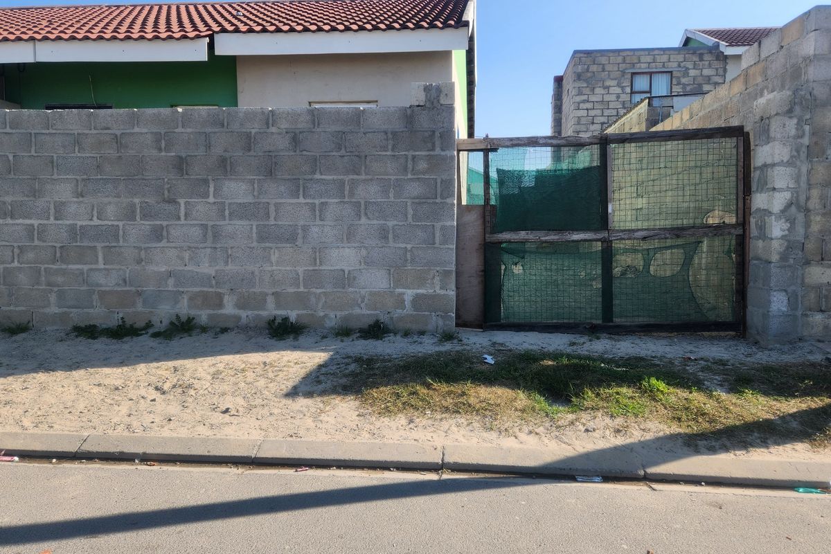 Street view of a residential property featuring an unfinished concrete block boundary wall and a basic metal gate entrance.