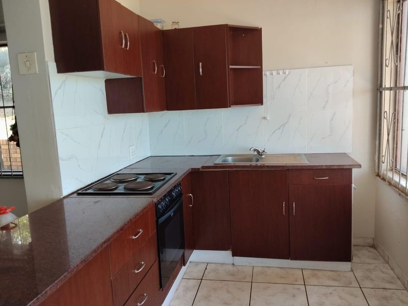 A functional kitchen featuring dark wood-look cabinetry, stone-effect countertops, built-in oven and hob, and tiled splashbacks in a clean, empty space.