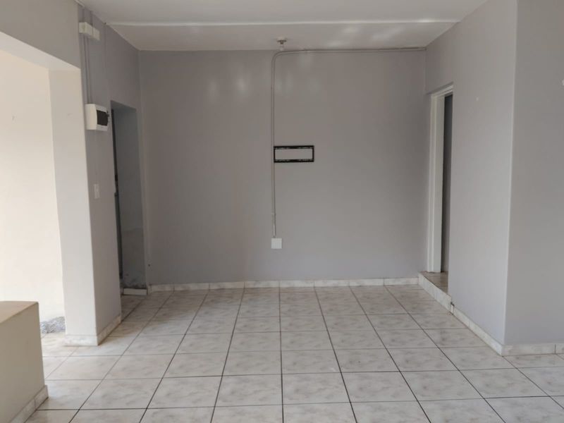 An empty living area featuring neutral tiled flooring and exposed electrical conduit, providing a blank canvas for potential interior design and renovation.