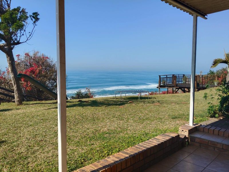 A covered patio area overlooking a spacious garden with expansive ocean views and a wooden deck platform.