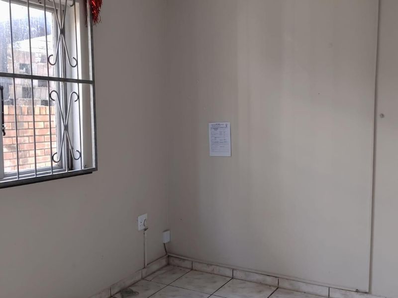 An empty bedroom featuring ceramic floor tiles, a window with a security gate, and neutral wall finishes.