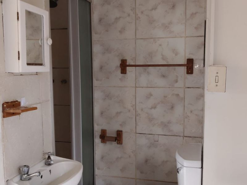 A compact bathroom featuring a wall-mounted basin, a shower enclosure, and a toilet, finished with dated wall and floor tiling.