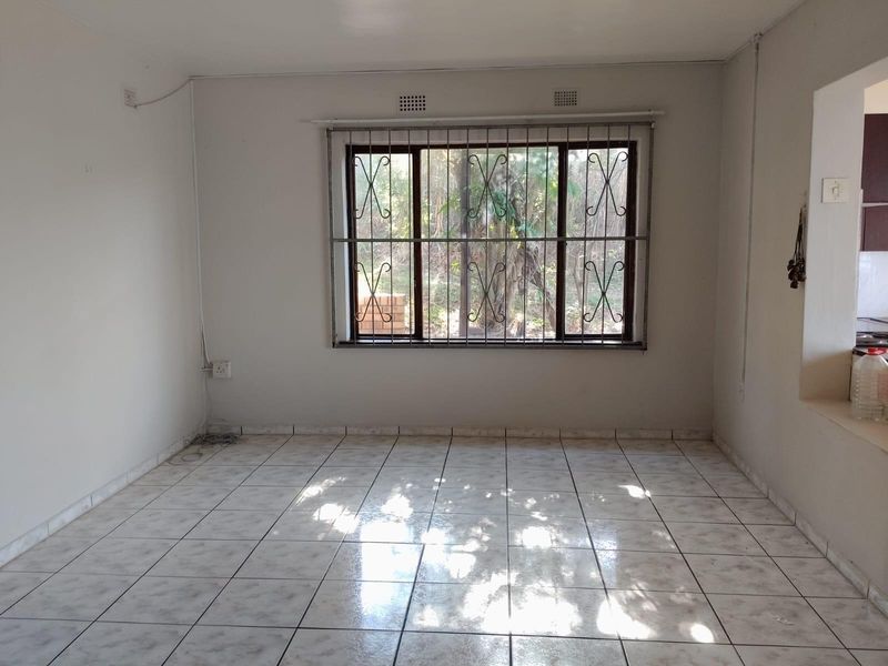 An empty living area featuring tiled flooring and a window fitted with security bars, offering a blank canvas for interior design.