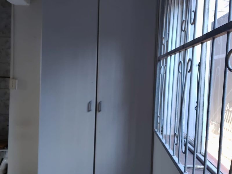 A simple bedroom featuring a built-in wardrobe, tiled flooring, and a window fitted with security bars.
