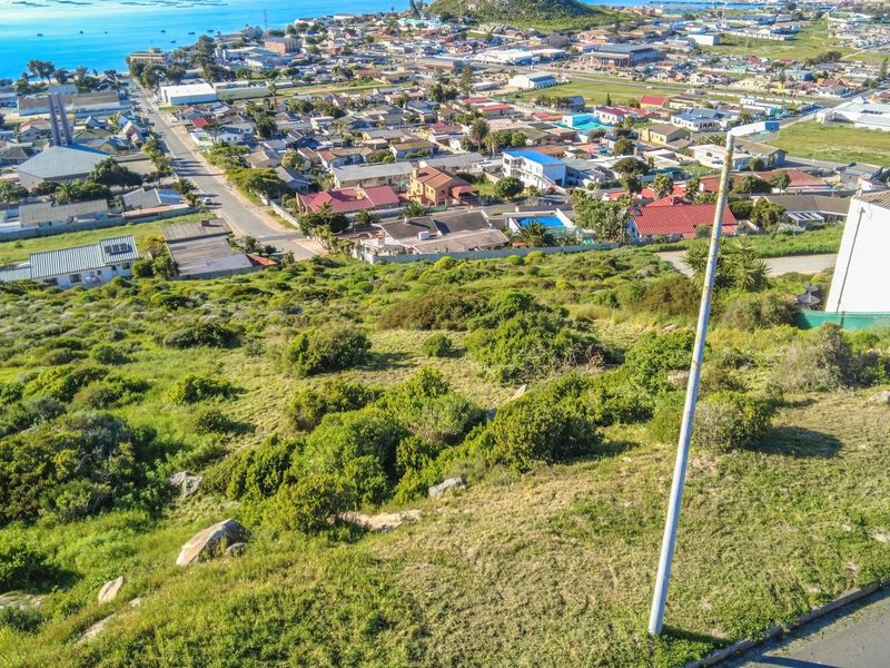 An elevated aerial view of a vacant residential plot featuring natural vegetation, overlooking the surrounding coastal town and ocean.