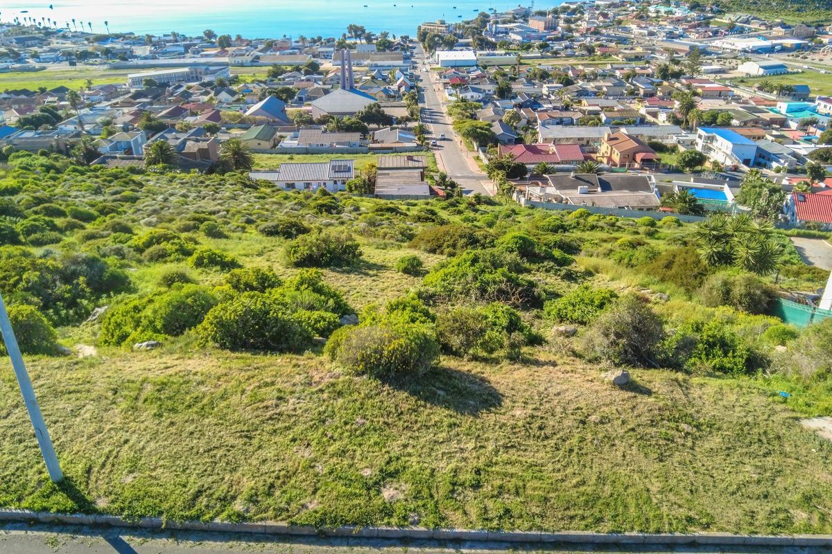 An elevated aerial view of a sloped, undeveloped residential plot overlooking the town and coastline.