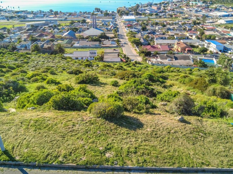 An elevated aerial view of a sloped, undeveloped residential plot overlooking the town and coastline.