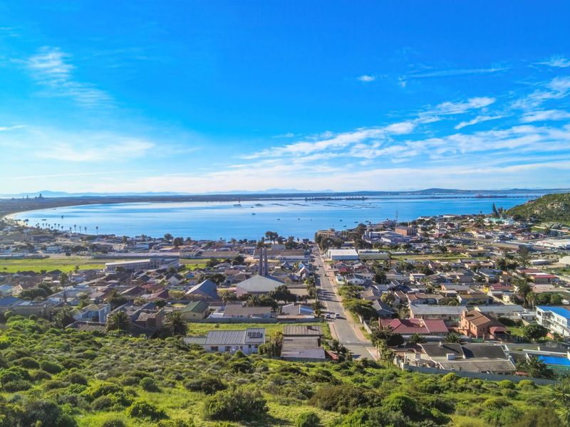 An elevated aerial view overlooking the coastal town, surrounding residential area, and the expansive bay in the distance.