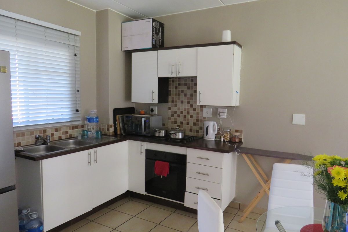 Compact kitchen featuring white cabinetry, dark laminate countertops, mosaic tile backsplash, built-in oven, gas hob, and ceramic floor tiles.