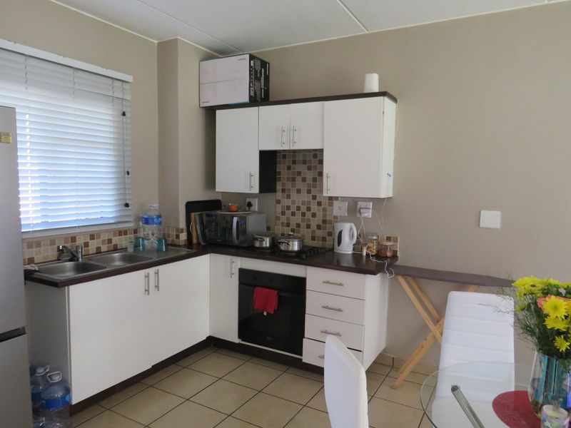 Compact kitchen featuring white cabinetry, dark laminate countertops, mosaic tile backsplash, built-in oven, gas hob, and ceramic floor tiles.