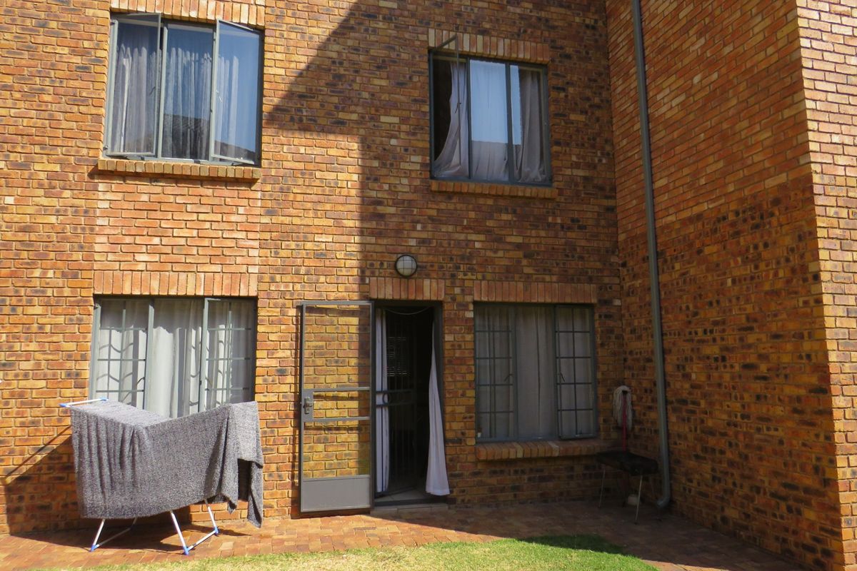 Rear exterior view of a face brick apartment building featuring a paved patio area and security access door.