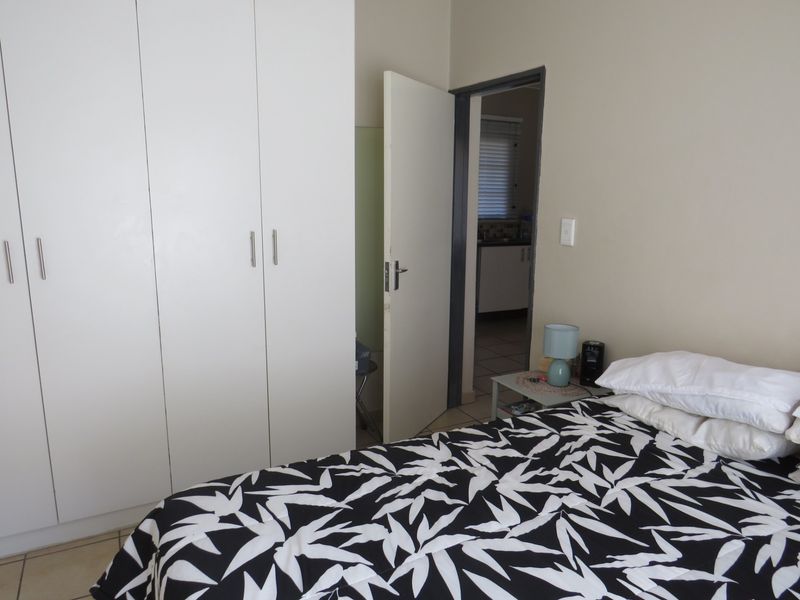 A bedroom featuring built-in cupboards and tiled flooring, with a doorway leading to an adjacent kitchen area.