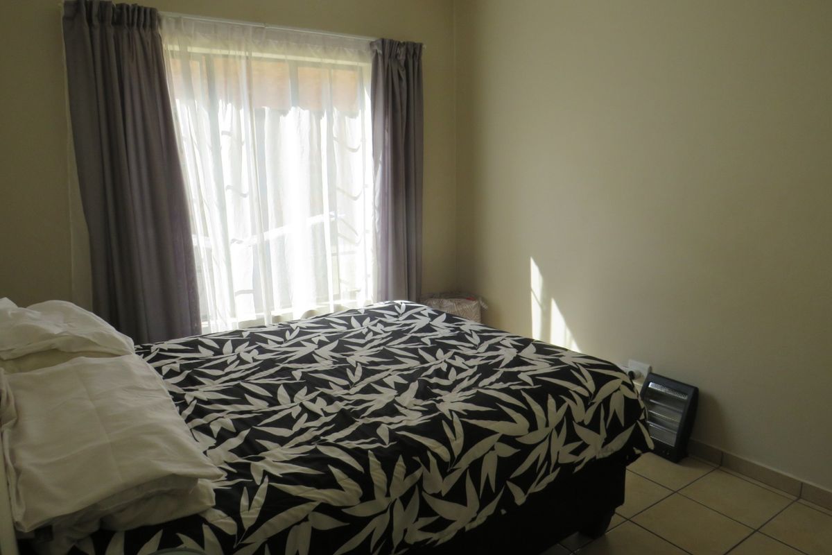 A functional bedroom featuring tiled flooring and natural light from a large window with curtain treatments.