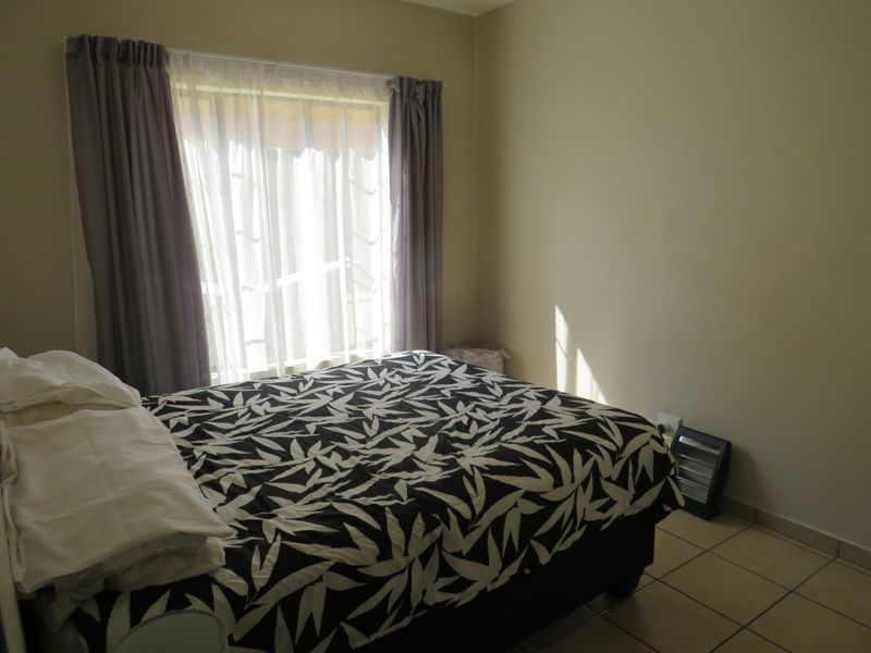 A functional bedroom featuring tiled flooring and natural light from a large window with curtain treatments.
