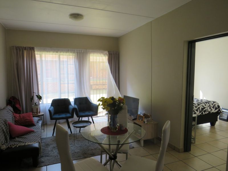 Open-plan living and dining area featuring tiled flooring and large windows with security gates, providing access to an adjacent bedroom.
