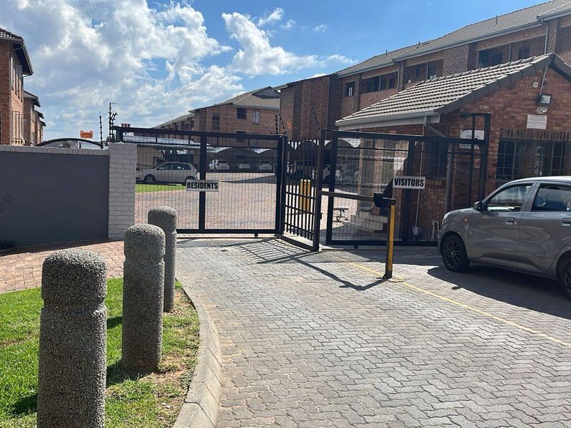 Secure apartment complex entrance featuring a brick facade, paved driveway, and controlled access gates for residents and visitors.