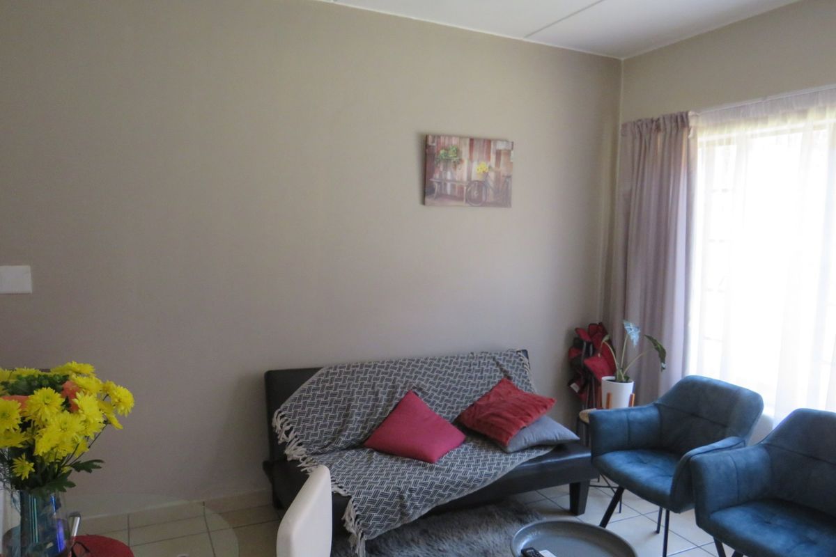A bright living room featuring neutral wall tones, tiled flooring, and a large window allowing for ample natural light.