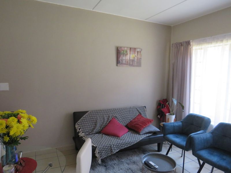 A bright living room featuring neutral wall tones, tiled flooring, and a large window allowing for ample natural light.