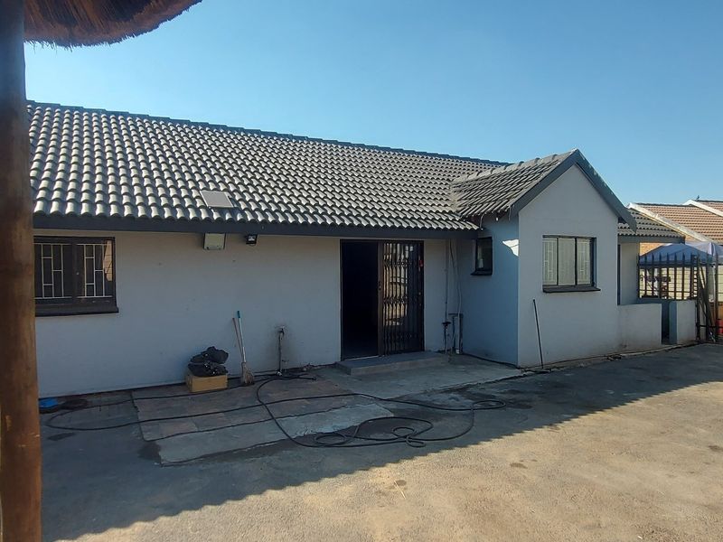 Rear view of the house featuring a tiled roof, security gates, and a paved driveway area.