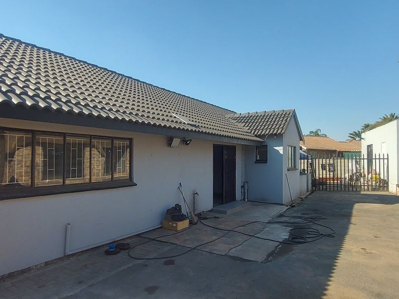 Rear exterior view of the house featuring a tiled roof, security bars on windows, and a paved driveway area with a metal gate.