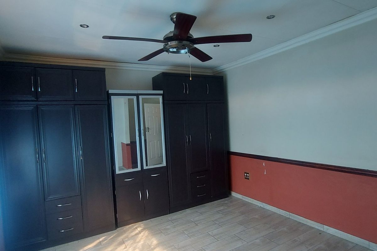 Spacious bedroom featuring extensive dark wood built-in cabinetry, tiled flooring, and a ceiling fan, offering a functional layout ready for personalization.