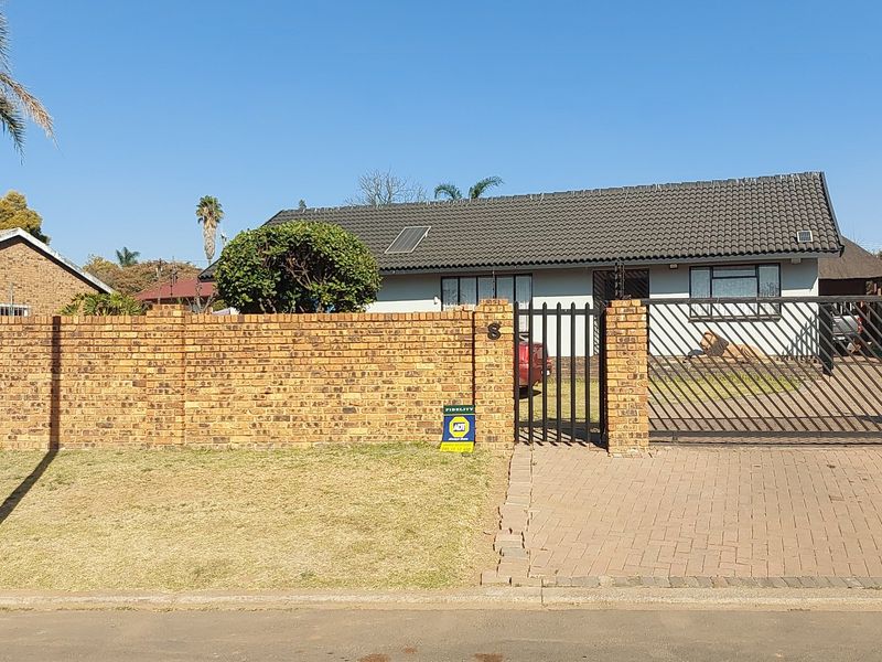 Front view of a single-story house featuring a brick boundary wall, paved driveway, metal sliding gate, and a tiled roof with a solar panel.
