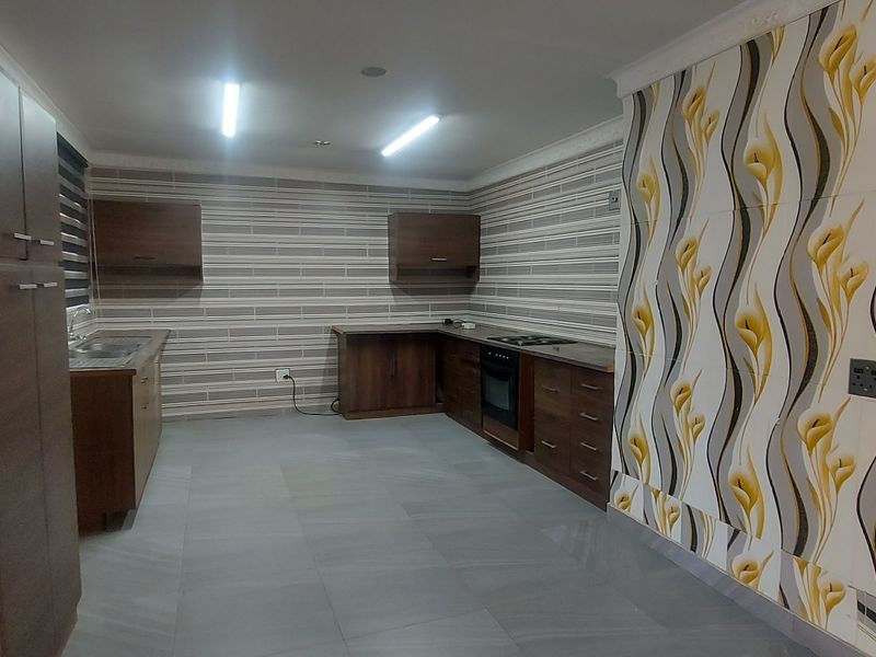 A spacious kitchen featuring dark wood cabinetry, built-in oven and hob, tiled flooring, and decorative feature wall tiling.
