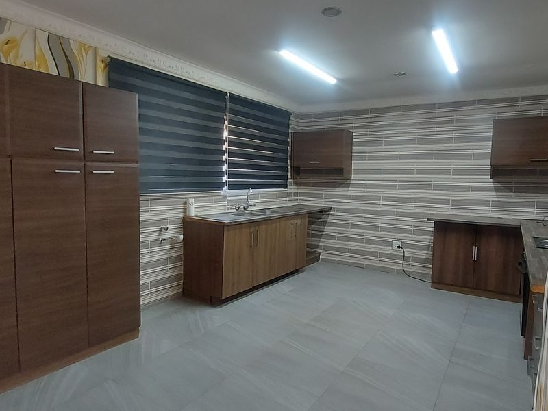 A spacious, empty kitchen featuring modern wood-finish cabinetry, tiled flooring, and neutral wall finishes, offering a clean canvas for personalization.