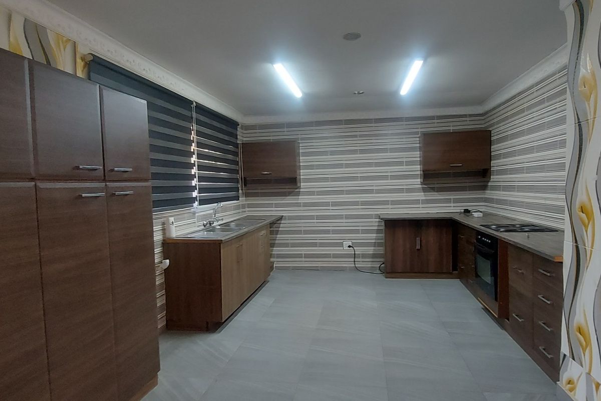 Spacious kitchen featuring extensive built-in cabinetry, integrated oven and hob, double sink, and modern tiled flooring with decorative wall finishes.