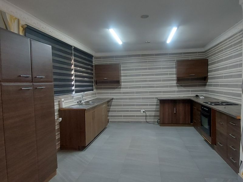 Spacious kitchen featuring extensive built-in cabinetry, integrated oven and hob, double sink, and modern tiled flooring with decorative wall finishes.