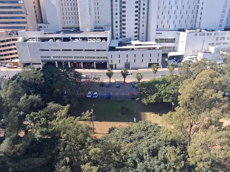 An elevated aerial view showing a landscaped garden area, adjacent parking lot, and surrounding urban infrastructure.