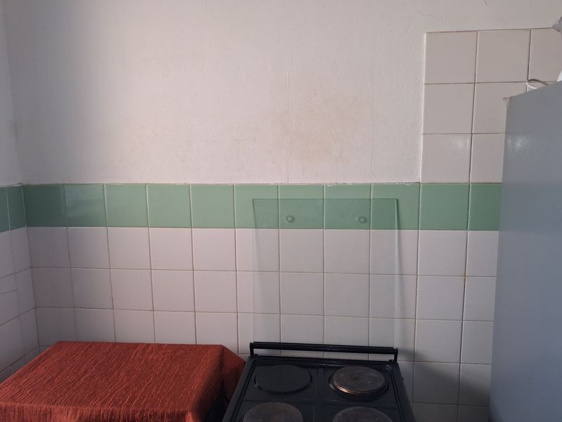 A kitchen area featuring a built-in electric stove and dated ceramic wall tiling, requiring cosmetic updates to improve the overall aesthetic.
