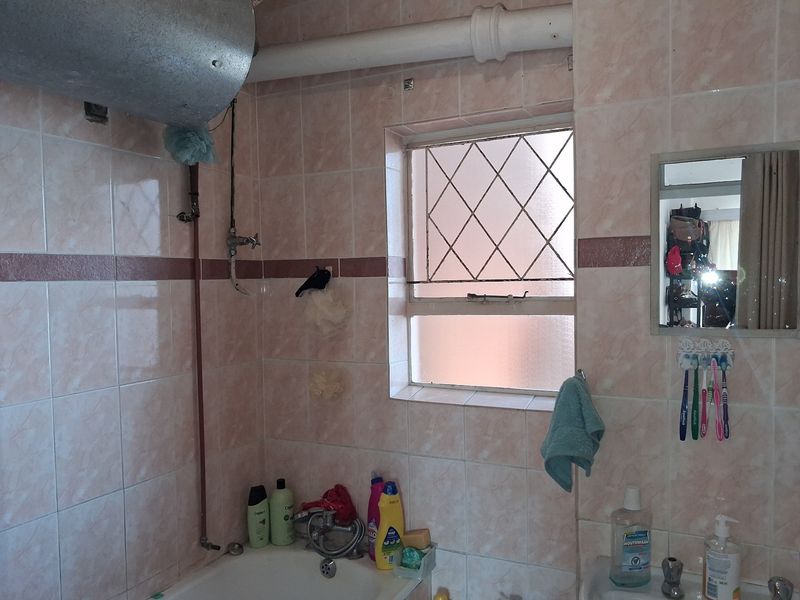 A dated bathroom featuring tiled walls, a bathtub with mixer tap, and exposed plumbing and water heater infrastructure.