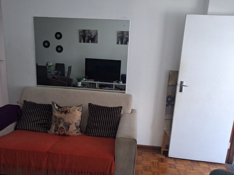 A living room area featuring classic parquet flooring, a large wall-mounted mirror, and a standard internal door.
