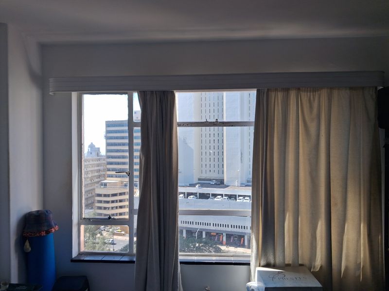 A bedroom interior featuring a large metal-framed window with city views and an integrated curtain rail system.