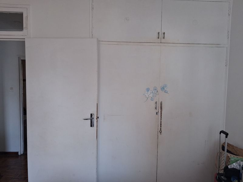 Bedroom featuring built-in cupboards with overhead storage and a standard internal door, showing signs of wear and requiring cosmetic updates.