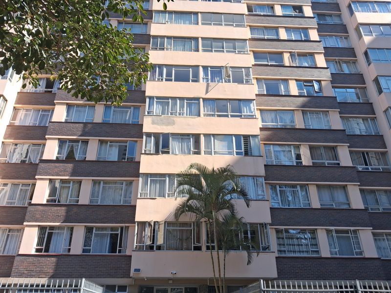 Front elevation of a multi-story apartment building featuring a brick and rendered facade with numerous casement windows and perimeter security fencing.