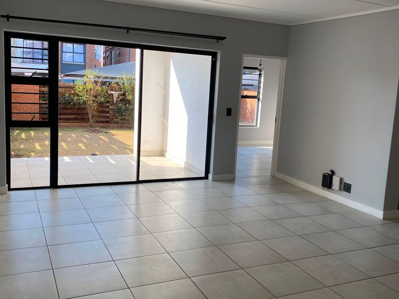 Spacious, light-filled living area featuring neutral tiled flooring, modern track lighting, and large sliding glass doors opening onto a private patio and garden.