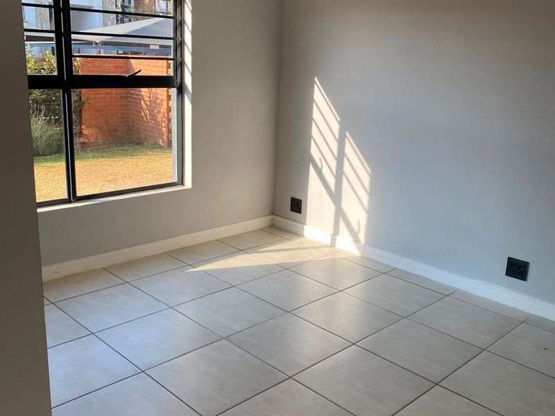 A bright, empty bedroom featuring neutral tiled flooring, clean grey walls, and a large window with black frames, offering a blank canvas for styling.