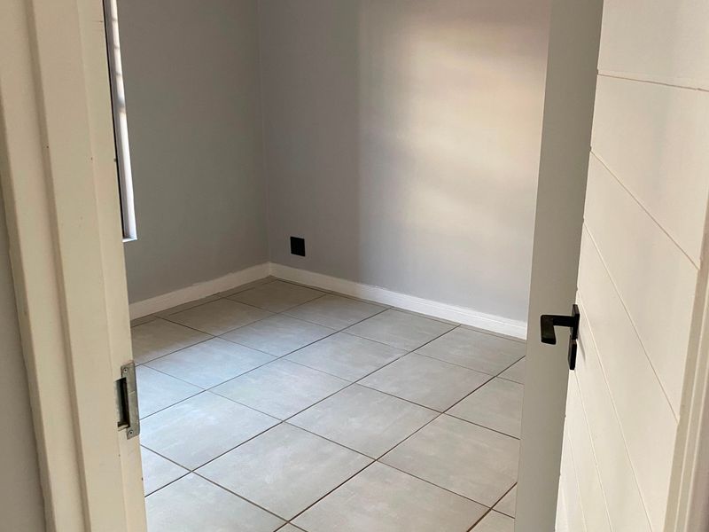 A clean, empty bedroom featuring neutral grey walls, large format floor tiles, and a modern pendant light fixture.