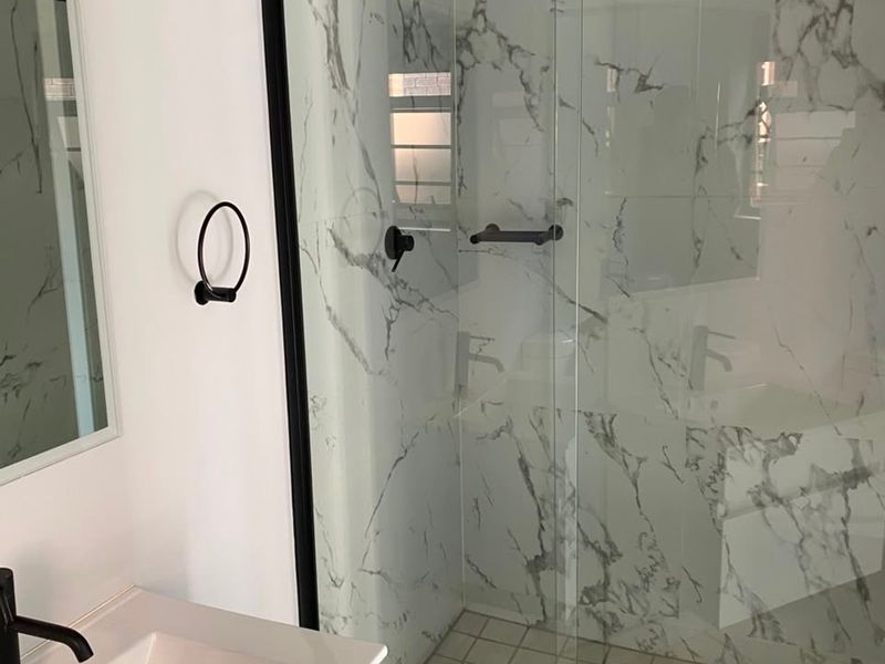 Modern bathroom featuring a walk-in shower with marble-look wall tiles, black fixtures, and a sleek vanity basin.