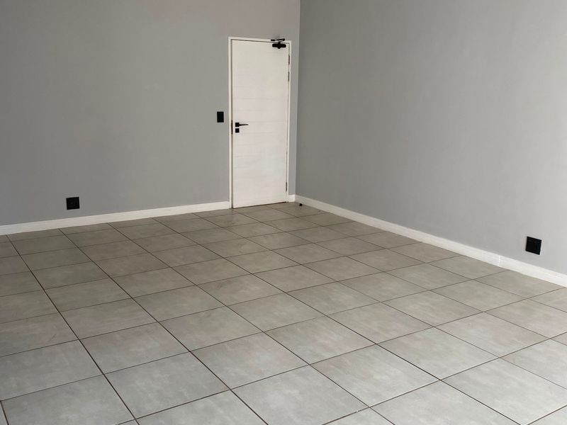 A bright, empty living area featuring neutral grey walls, modern track lighting, and large format floor tiles throughout.