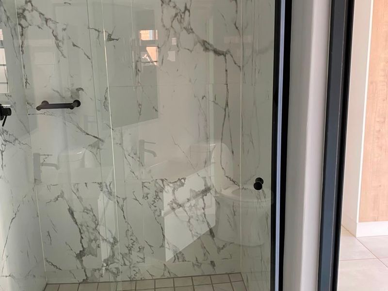 Modern bathroom featuring a walk-in shower with marble-look wall tiles, black frame detailing, and a square floor drain.