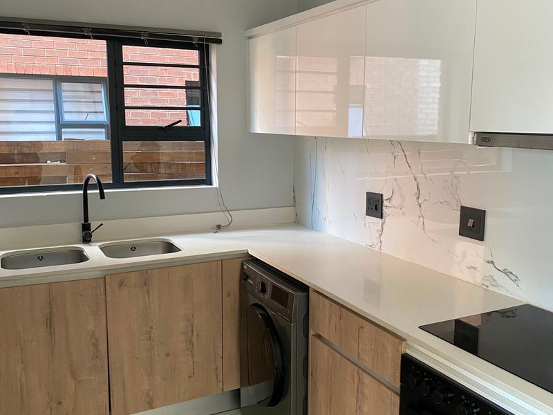 Modern kitchen featuring sleek laminate cabinetry, stone countertops, marble-look splashback, integrated oven, and hob with a double sink and tiled flooring.