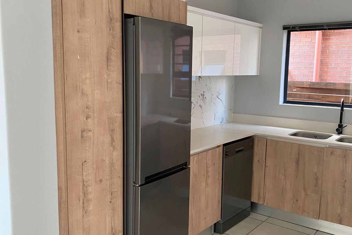 Modern kitchen featuring wood-grain and white cabinetry, marble-look splashback, integrated dishwasher, and contemporary black fixtures with tiled flooring.