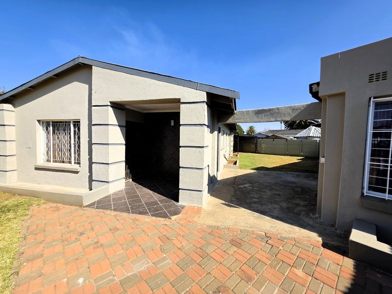 Rear exterior view of the property featuring a paved driveway, covered patio area, and a secure backyard with concrete boundary walls.