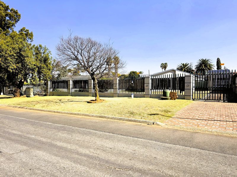 Front view of the property featuring a well-maintained lawn, secure perimeter fencing with brick pillars, and a paved driveway entrance.