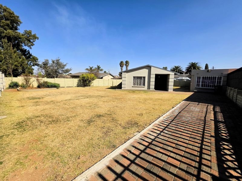 Spacious rear garden featuring a paved driveway, precast concrete boundary walls, and a detached outbuilding with security bars on the windows.
