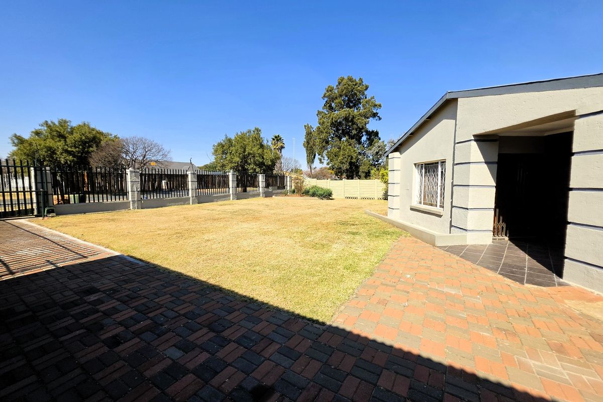 A spacious rear garden featuring a paved patio area, well-maintained lawn, and secure perimeter fencing.