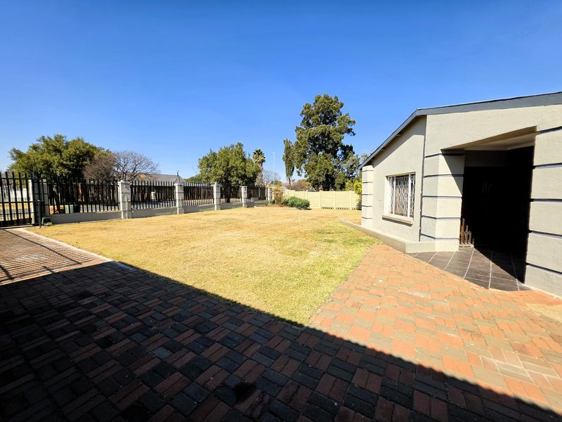 A spacious rear garden featuring a paved patio area, well-maintained lawn, and secure perimeter fencing.
